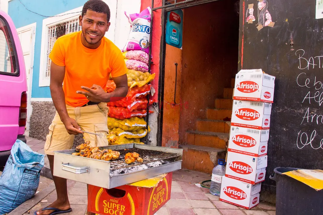 Smiling street vendor grilling chicken in Mindelo